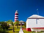 Red and white candy cane striped lighthouse on Elbow Cay, Abaco, Bahamas, Hope Town. Storage shed with small boat are in the foreground. Copy space available in the clear blue sky.