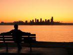 silhouette of a man sitting on a park bench watching the sun rise behind Seattle skyline.